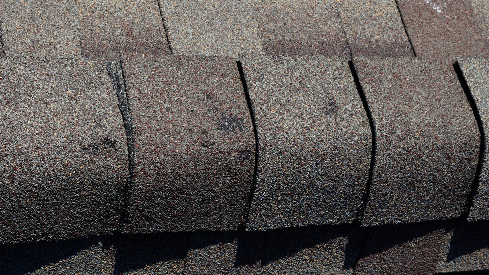 Sunlit asphalt roof topped with ridge cap shingles in brown tones