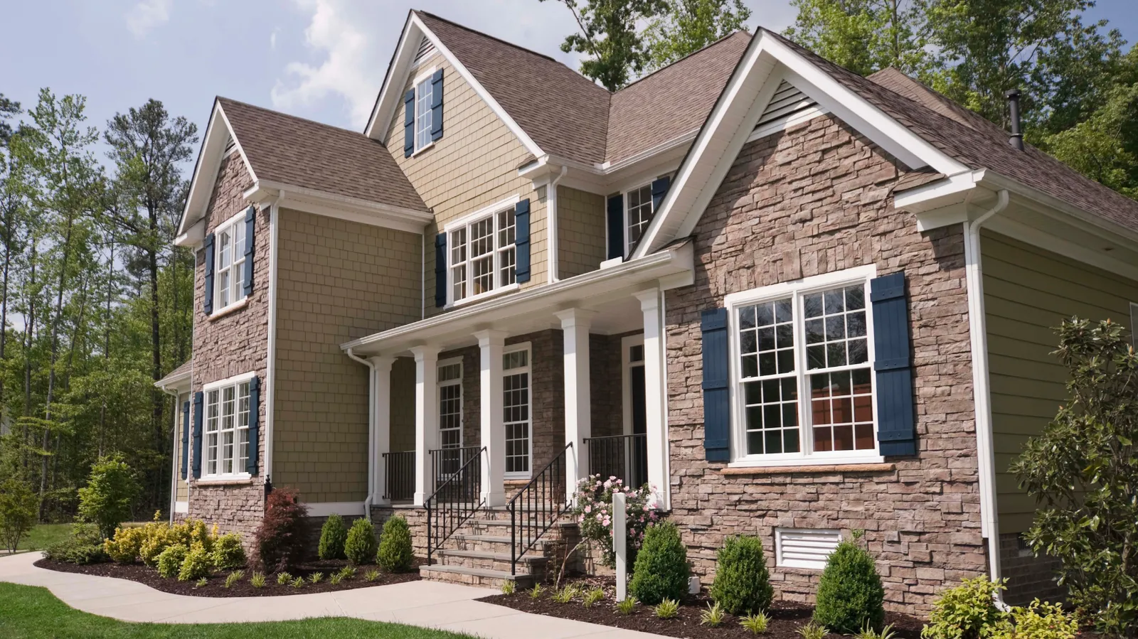 Two-story home with stacked stone and shake siding under a brown shingle roof
