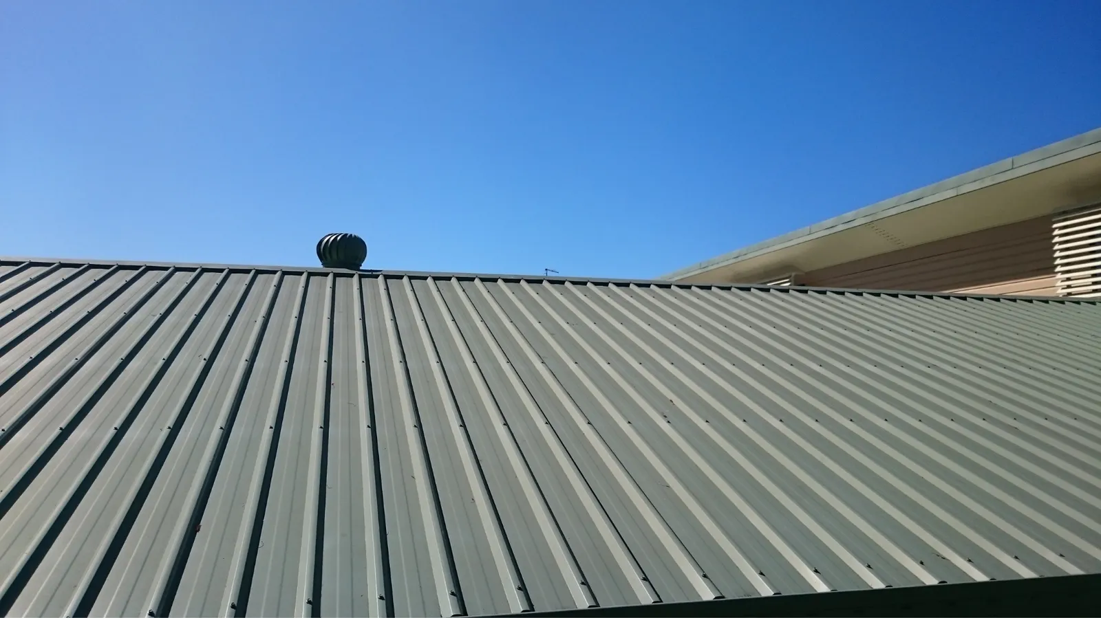 Clear blue sky above a corrugated metal roof with turbine vent