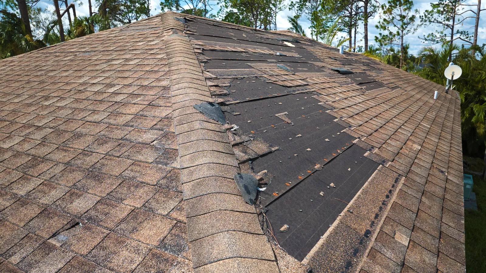 Shingles gone in large patches across a brown hip roof